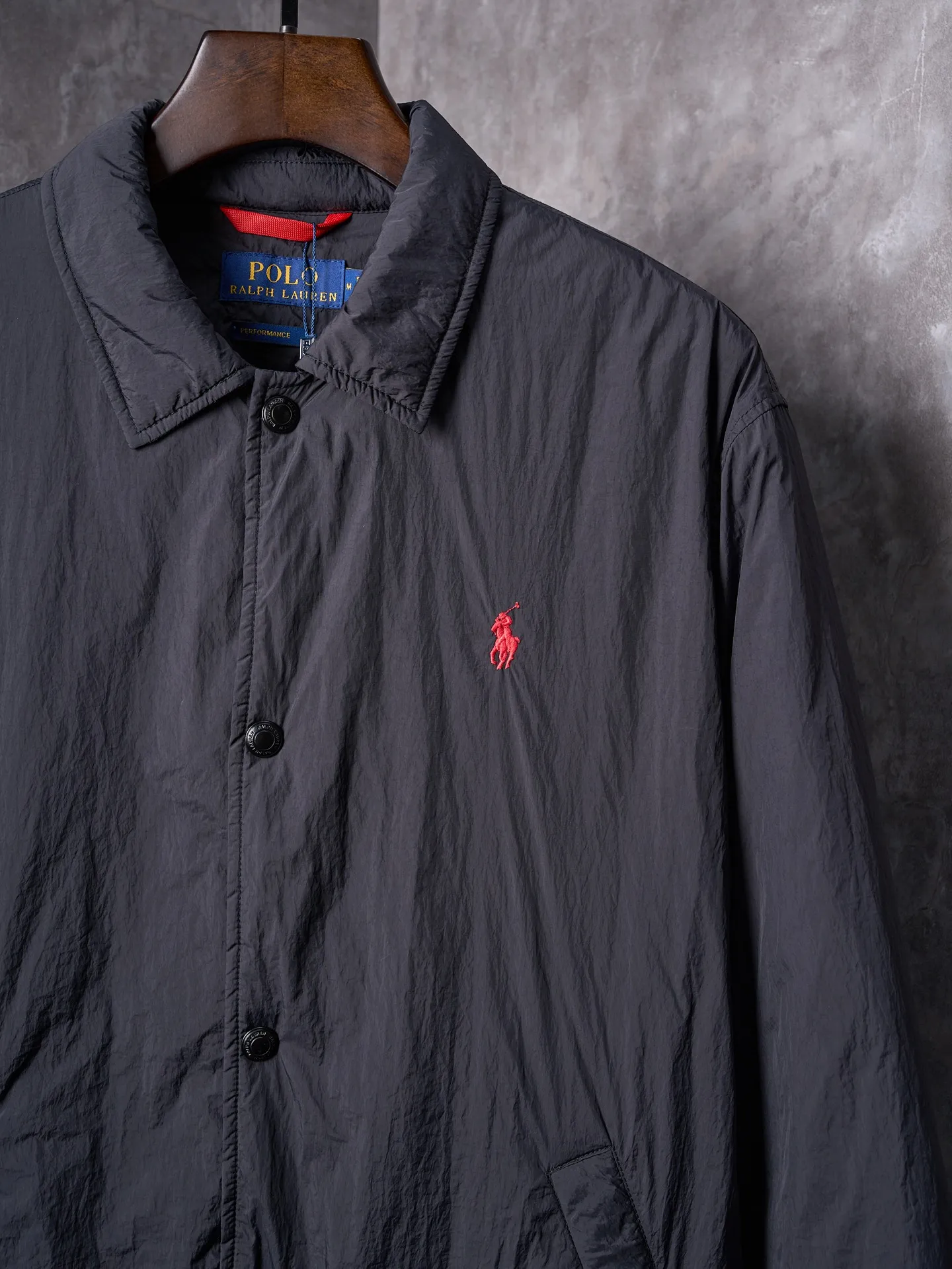 P640 Actual auction] Ralph Lauren/Ralph Lauren Pony Red Label lightweight cotton lapel coach jacket [Ready stock] S M L XL Material: high-density nylon taffeta Features: Density is about 210T-300T, smooth and slightly matte surface, excellent windproof and waterproof performance (with DWR water-repellent treatment), strong wrinkle resistance and easy care, in line with the positioning of American casual "durable and practical".  Color: Classic dark black, using vat dyeing process (dye penetrates into the fiber), the color fastness reaches ISO level 4 or above to avoid fading or color transfer after washing.  2. Lining fabric Material: Lightweight cotton-polyester blended lining (65% Polyester + 35% Cotton) Function: Reduce friction between the fabric and inner clothing, improve wearing smoothness; blended material has both breathability and durability to avoid the stuffy feeling of pure nylon lining.  Version and cutting process Version: Classic Coach Jacket, loose version, slightly dropped shoulder line (shoulder width is 1-2cm wider than the standard version), length to the hips, and slightly tapered straight sleeves, taking into account both freedom of movement and casual style. Embroidery technology: Polo horse logo on the left chest: flat satin stitch embroidery (satin embroidery), embroidery thread: 100% polyester high color fastness embroidery thread (the color number is consistent with the brand’s standard red color card), stitch density 12-15 stitches/cm, the outline of the horse logo is clear, and the details of the rider and horse are burr-free.  Embroidery positioning: precise positioning through the template (12cm from the neckline and 8cm from the placket) to ensure left and right symmetry and centering.  Topstitching technology: The seams of the body are made of double-needle flat seams (needle pitch 3cm/10 needles), the stitches are smooth and straight, the stitching color is dark black (the same color as the fabric), and the stitch width is 0.5cm, which enhances firmness while forming simple decorative lines.  1. Main body splicing, splicing of the front placket and body: The placket is made of double-layer folding + flat seam splicing, with a thickness of about 0.3cm to ensure that the buttons are not easily deformed when fixed; the edges of the placket are cut with a hot knife to avoid burrs.  Sleeve panels are spliced ​​to the body: the armholes are spliced ​​with round-head keyhole machine seams + flat seams. After splicing, the armholes have a natural curvature and no sense of tightness during movement; the height of the sleeves is about 8-10cm, which is in line with the loose characteristics of casual jackets.  Main button: black urea resin button, matte surface treatment, buttonholes are hand-made keyholes (6 strands of cotton thread, keyhole density 8 stitches/mm), the edges of the eyelets are smooth and without burrs.  Collar buttons: The first button on the collar is a hidden button (diameter 12mm), which prevents the collar from opening and improves the neatness of wearing.